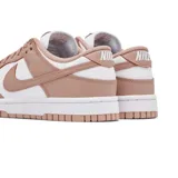 Championes Nike Dunk Low con diseño bicolor en blanco y rosa viejo. Presentan una silueta clásica de perfil bajo, con paneles de cuero, perforaciones en la puntera para mayor ventilación y suela de goma resistente.