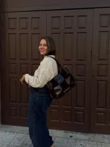 Cartera de hombro confeccionada en cuero y gamuza con diseño de damero, combinando paneles de texturas lisas y aterciopeladas. Presenta una manija trenzada y detalles de costuras artesanales en los laterales.