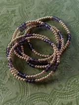 Pulsera elástica compuesta por una alternancia de cuentas metálicas doradas y cristales facetados de color violeta.