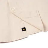 Camisa de manga larga color arena con cuello clásico, cierre frontal con botones, dos bolsillos de parche en el pecho con solapa y logo de Caterpillar en el bolsillo derecho.