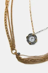 Pack de tres collares superpuestos de metal en tonos dorado y plateado. El collar más corto tiene un dije colgante en forma de reloj ovalado con piedras de colores. El collar intermedio tiene un dije colgante en forma de reloj redondo con marco floral. El collar más largo consiste en múltiples cadenas finas, algunas con cuentas, y un dije colgante en forma de estrella de múltiples puntas.