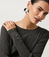 Suéter de punto color rosado, con cuello barco, mangas largas y puños con botones decorativos. El dobladillo también es acanalado.