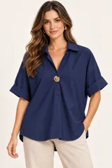 Camisa de algodón color azul marino, de corte holgado y diseño versátil. Cuenta con cuello camisero, escote en V pronunciado con detalle de botón dorado grande, mangas cortas con vuelta y dobladillo redondeado más largo en la parte trasera.