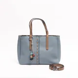 Cartera tipo tote de cuerina color celeste, con detalles y asas de mano en color tostado. Presenta un llavero decorativo colgante con cuentas de colores, costuras decorativas frontales y una correa ajustable y desmontable.