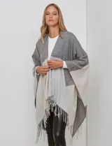 Ruana tejida con diseño colorblock en tonos de gris y beige, con flecos en el borde inferior.