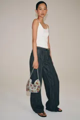 Bolso de hombro plateado cubierto de abalorios y cuentas, decorado con apliques florales tridimensionales en tonos verde y fucsia. Cuenta con un asa corta para el hombro, cierre de clip imantado y bolsillo interior con cremallera.