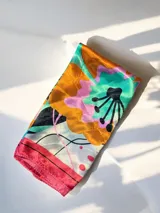 Pañuelo cuadrado de seda con estampado floral multicolor que combina tonos rojos, amarillos, azules y fucsias sobre fondo blanco, con borde rojo.