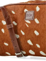 Bandolera compacta de cuero con pelo, con estampado animal print simil ciervo en tonos marrón y blanco. Cuenta con detalles de ribetes en cuero liso marrón, correa ajustable y un aplique frontal con el logo de la marca grabado.