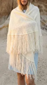 Ruana color crema tejida en punto bouclé, de forma triangular con flecos largos en los bordes.