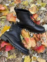Botas de caña media de cuero color negro, con acordonado frontal y suela dentada. Presentan un detalle en tono claro en el talón.