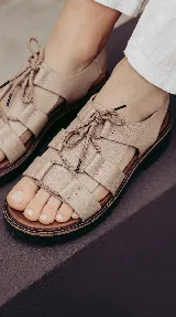 Sandalia de cuero color visón con tiras anchas entrelazadas, cordones ajustables en el empeine, suela dentada y base de goma.