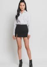Mini falda negra de corte recto y tiro alto, con un pequeño tajo lateral en el frente.