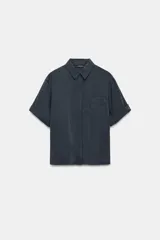Camisa de corte fluido confeccionada en mezcla de modal, con cuello solapa, manga corta con dobladillo y bolsillo de plastrón en el delantero. Presenta cierre frontal con botones ocultos por tapeta y aberturas laterales en el bajo.