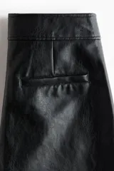 Pantalón de tejido revestido con acabado efecto cuero, de corte recto y tiro medio. Presenta cierre frontal con cremallera, pretina con botón oculto, bolsillos laterales al bies y costura horizontal visible sobre las rodillas.