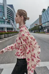 Blusa de cuello subido y manga larga con estampado floral en tonos rosados. Presenta un diseño con volantes en el pecho y a lo largo de las mangas, con cierre posterior mediante botones ocultos.