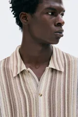 Camisa de manga corta con cuello inglés y botones frontales, confeccionada en tejido de punto pointelle con patrón de rayas verticales en tonos tierra y beige.