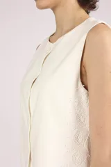 Chaleco blanco sin mangas, con cuello redondo y cierre frontal de botones. El chaleco tiene un corte recto y ligeramente holgado.