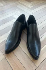 Zapatos tipo botineta de cuero vacuno color negro con textura grabada tipo reptil, diseño de punta fina y cierre trasero.