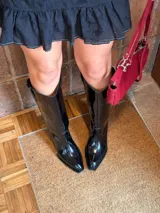 Botas tejanas altas de cuero charol color negro, con punta fina y diseño de caña alta con tiradores laterales.