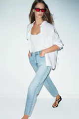 Jeans de denim azul claro lavado, tiro alto, corte Mom Fit con pierna recta y largo tobillero. Presenta cinco bolsillos y cierre frontal con cremallera y botón.