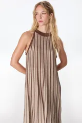 Vestido largo de tejido de punto fino con Lurex, de silueta en A, sin manga y con cuello halter. Presenta un patrón de rayas verticales en tonos beige y marrón, con aumentos en el tejido para mayor soltura.