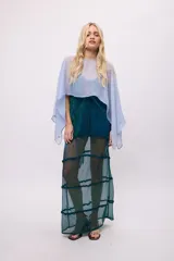 Poncho corto de chiffon color amarillo verdoso con textura plisada y brillo metálico. Presenta un cuello redondo y mangas amplias tipo capa.