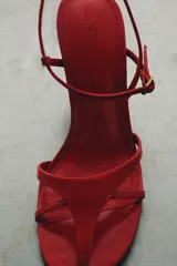 Sandalia de piel color rojo con diseño de tiras finas en la parte delantera. Cuenta con cierre de pulsera al tobillo mediante hebilla metálica y tacón de altura media en color negro.