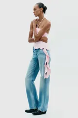 Top negro de cuello halter con lazada, escote recto y hombros descubiertos. Presenta un volante asimétrico en el lateral.