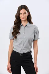 Camisa celeste rayada de manga corta, con cuello camisero y cierre frontal con botones. Presenta un corte entallado y un pequeño detalle de placa metálica en el borde inferior.