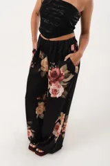 Pantalón palazzo negro con estampado floral en tonos rosa, naranja y amarillo. Tiene cintura alta con elástico.