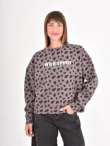 Buzo de cuello redondo y manga larga, con diseño holgado. Presenta un estampado de manchas oscuras sobre fondo beige y una estampa frontal con el texto 'WILD SPIRIT EST. 1970'.