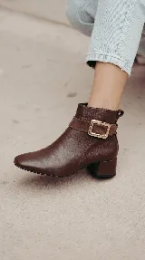 Bota corta de cuero color chocolate, con diseño minimalista, taco cuadrado de 4 cm y una hebilla metálica decorativa en el tobillo sobre una banda de gamuza.