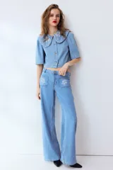 Blusa corta de denim de algodón con cuello Peter Pan bordado, mangas cortas abullonadas y cierre frontal con botones.