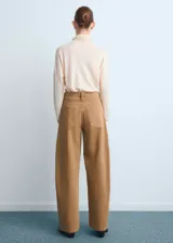 Pantalón tipo jeans de corte wide leg y tiro medio, confeccionado en denim de algodón color tostado. Presenta diseño de cinco bolsillos, cierre frontal con botón y cremallera, y costuras reforzadas.