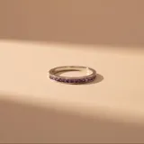 Anillo tipo alianza sin fin, confeccionado en plata 925, con engaste de circonias cuadradas en color lila a lo largo de toda la circunferencia.