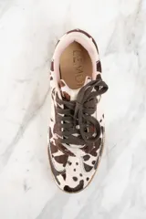 Zapatillas bajas con estampado de vaca en tonos marrón y blanco, con cordones marrones y suela de goma color caramelo.