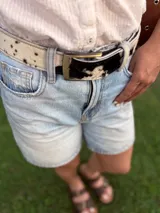 Cinto de cuero con forro de cuero, estampado animal print de vaca en blanco y negro, con hebilla metálica rectangular color bronce y broche suizo.