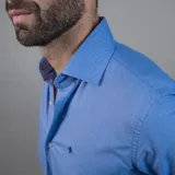 Camisa de vestir celeste de manga larga, con cuello clásico y botones blancos. Presenta un logo bordado en azul oscuro en el pecho.