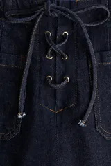 Jean de tiro alto en denim azul oscuro, con corte acampanado desde la rodilla. Presenta un diseño con cordones frontales para ajuste en la cintura, bolsillos delanteros y traseros, y costuras a contratono.