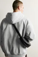Bolso de hombro pequeño color negro con acabado liso, diseño semilunar y costura central. Cuenta con compartimento principal con cierre de cremallera, bolsillo interior con cierre y asa de hombro ajustable con hebilla.