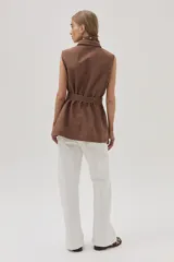 Chaleco largo marrón de algodón con cuello camisero, cierre frontal con botones, bolsillos laterales y lazo ajustable en la cintura.