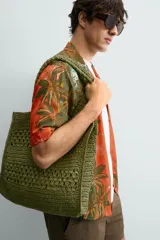 Camisa de corte relajado confeccionada en tejido fluido con mezcla de viscosa y lino. Presenta cuello bowling, manga corta y cierre frontal con botones. Diseño con estampado floral en tonos verdes y naranjas.