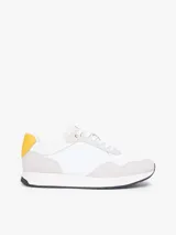 Zapatillas de estilo runner de Tommy Hilfiger, confeccionadas en una mezcla de cuero y textil en color blanco con detalles en gris claro y un panel amarillo en el talón. Presentan cordones blancos y suela de goma con base oscura.