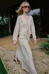 Falda midi de color crudo, con diseño combinado que presenta una parte superior de crochet con motivos florales y una parte inferior de tela fluida con textura arrugada. Incluye forro interior y cierre lateral con cremallera oculta.