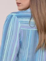 Blusa de gasa de la marca Zac & Rachel, con estampado de rayas verticales en tonos azules, celestes y lilas. Presenta cuello a la base con escote en V, abertura central con botones, detalle plisado en el frente y mangas de largo regulable con presilla y botón.