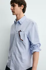 Camisa de corte regular fit confeccionada en tejido de algodón tipo Oxford. Presenta cuello abotonado, manga larga con puños abotonados, bolsillo frontal en el pecho y cierre de botonadura central.