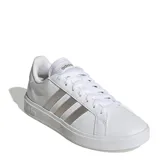 Championes urbanos Adidas modelo Grand Court Base 2.0, color blanco con las icónicas tres franjas laterales en tono gris metalizado. Presentan un diseño inspirado en los años 70 con suela tipo cupsole de caucho y cierre mediante cordones.