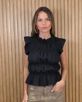Blusa sin mangas de color negro, con diseño fruncido mediante elásticos en el torso y cuello alto con volados.