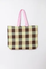 Tote bag de tela con diseño a cuadros en tonos marrón, beige y verde, tiras de hombro color rosado y la palabra "VOYAGE" estampada en el frente en color rosado.