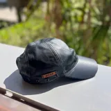 Gorra de cuero metalizado dorado, con ojales metálicos decorativos y etiqueta de marca aplicada en el lateral.